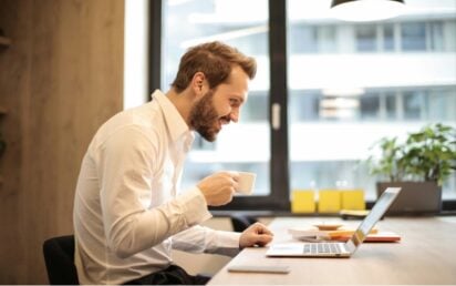 Man drinking coffee looking at laptop